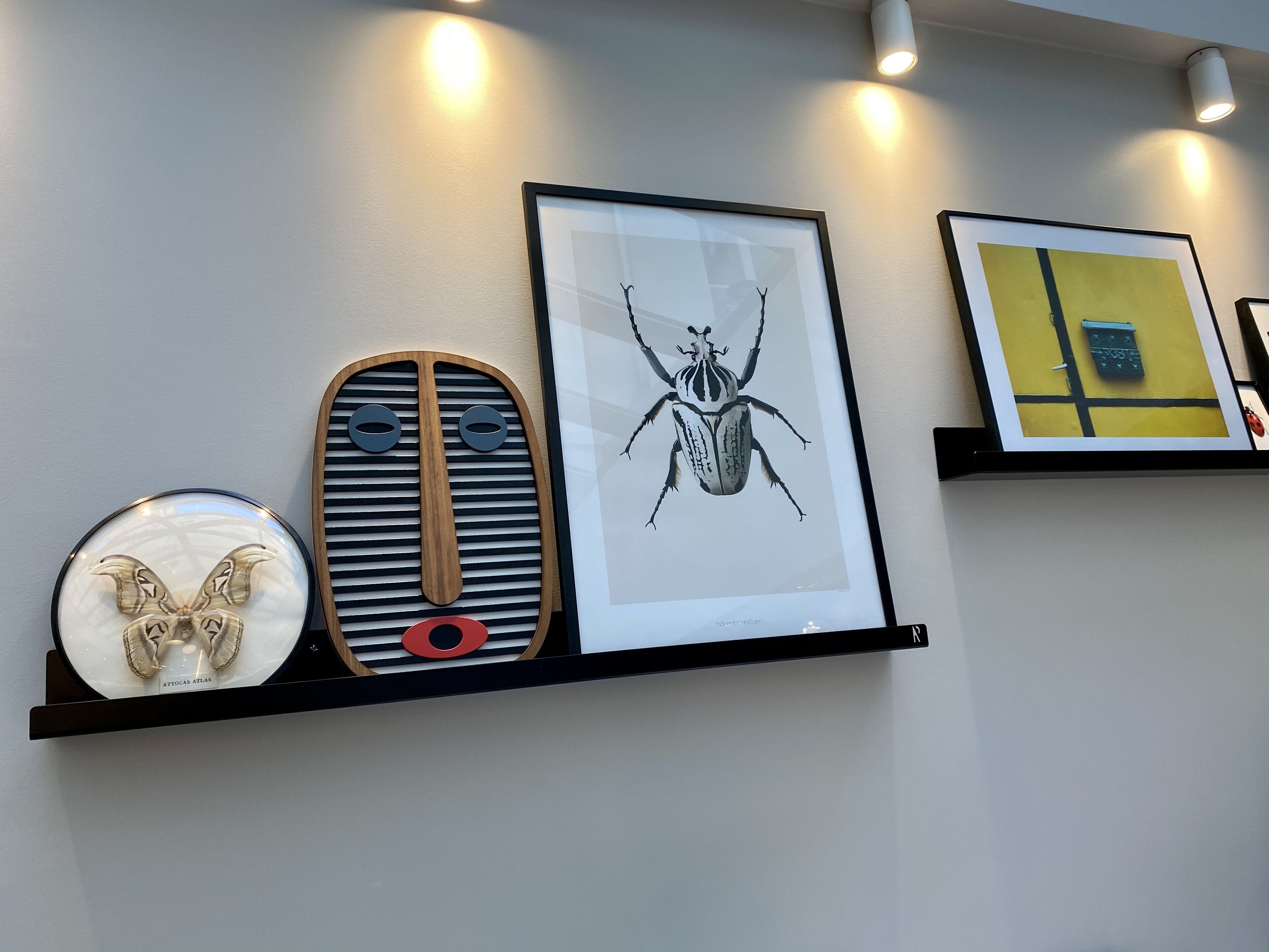 A wall with three framed artworks on a black shelf.