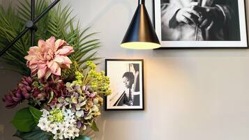 Un escritorio con un florero de flores, una lámpara de escritorio negra y dos fotografías enmarcadas en la pared.