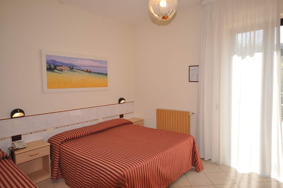 Een hotelkamer met twee bedden, een schilderij aan de muur, een bedlampje en een raam met gordijnen.