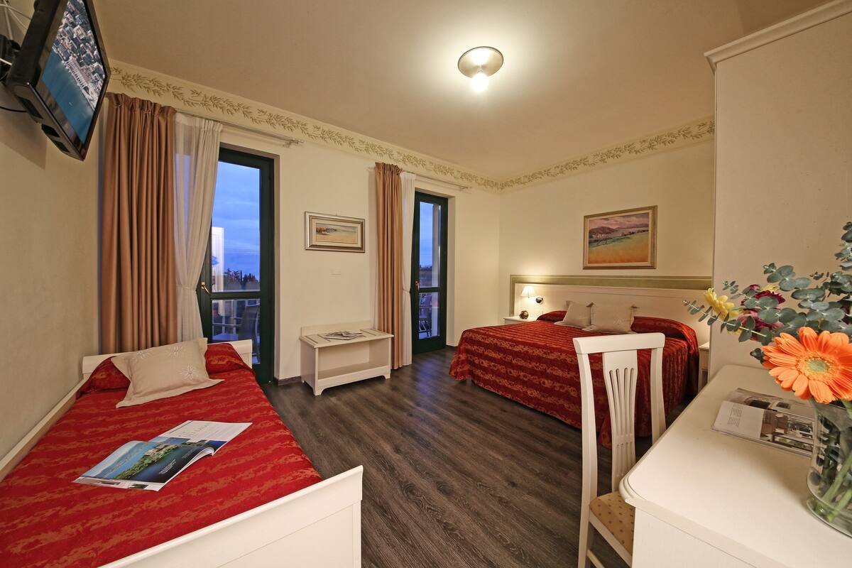 Een hotelkamer met twee bedden, een televisie, een bureau en een raam met gordijnen.