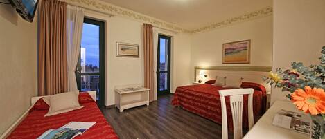 A hotel room with two beds, a TV, a desk, and a window with curtains.