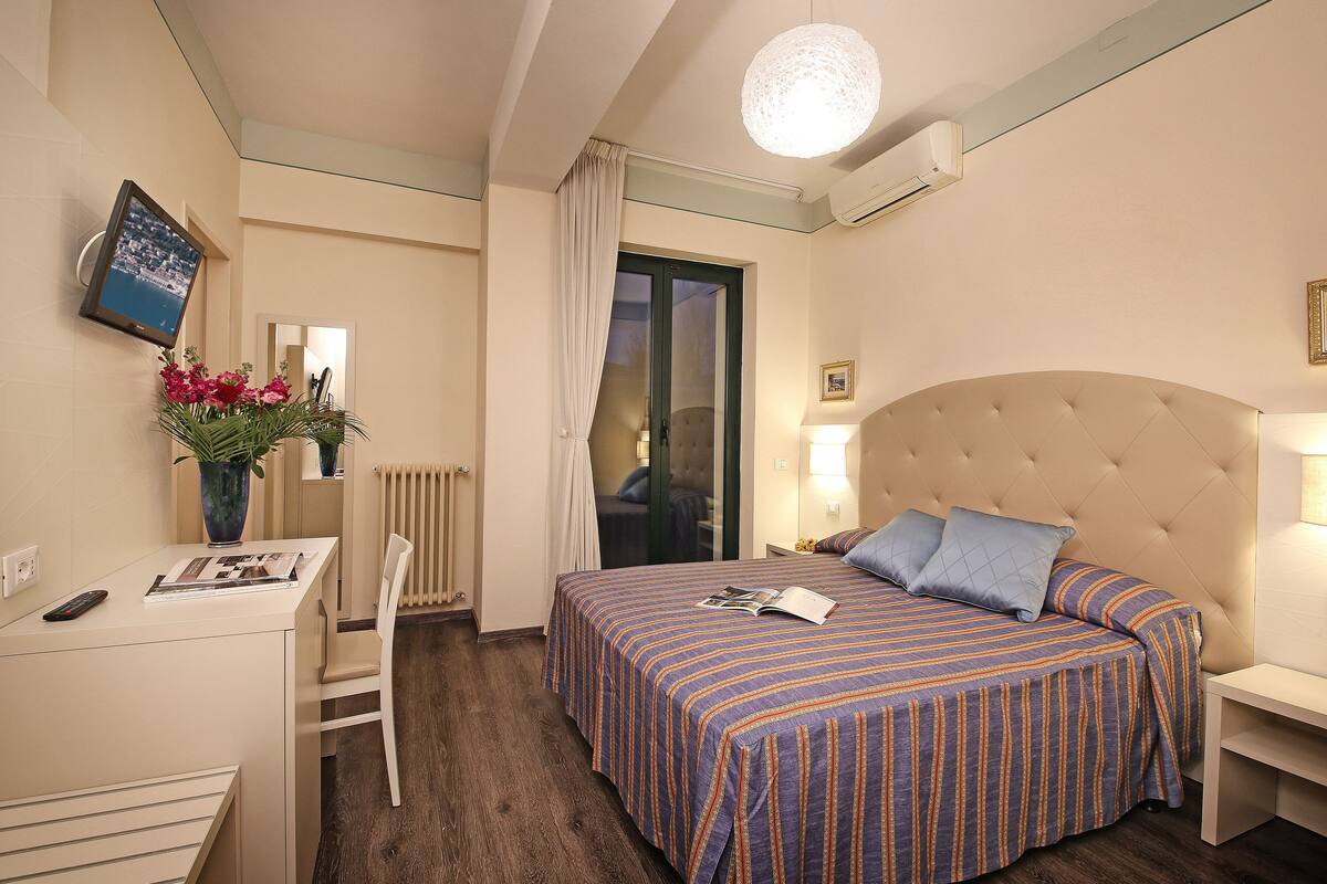 Een hotelkamer met een bed, een bureau, een stoel, een vaas met bloemen en een televisie.