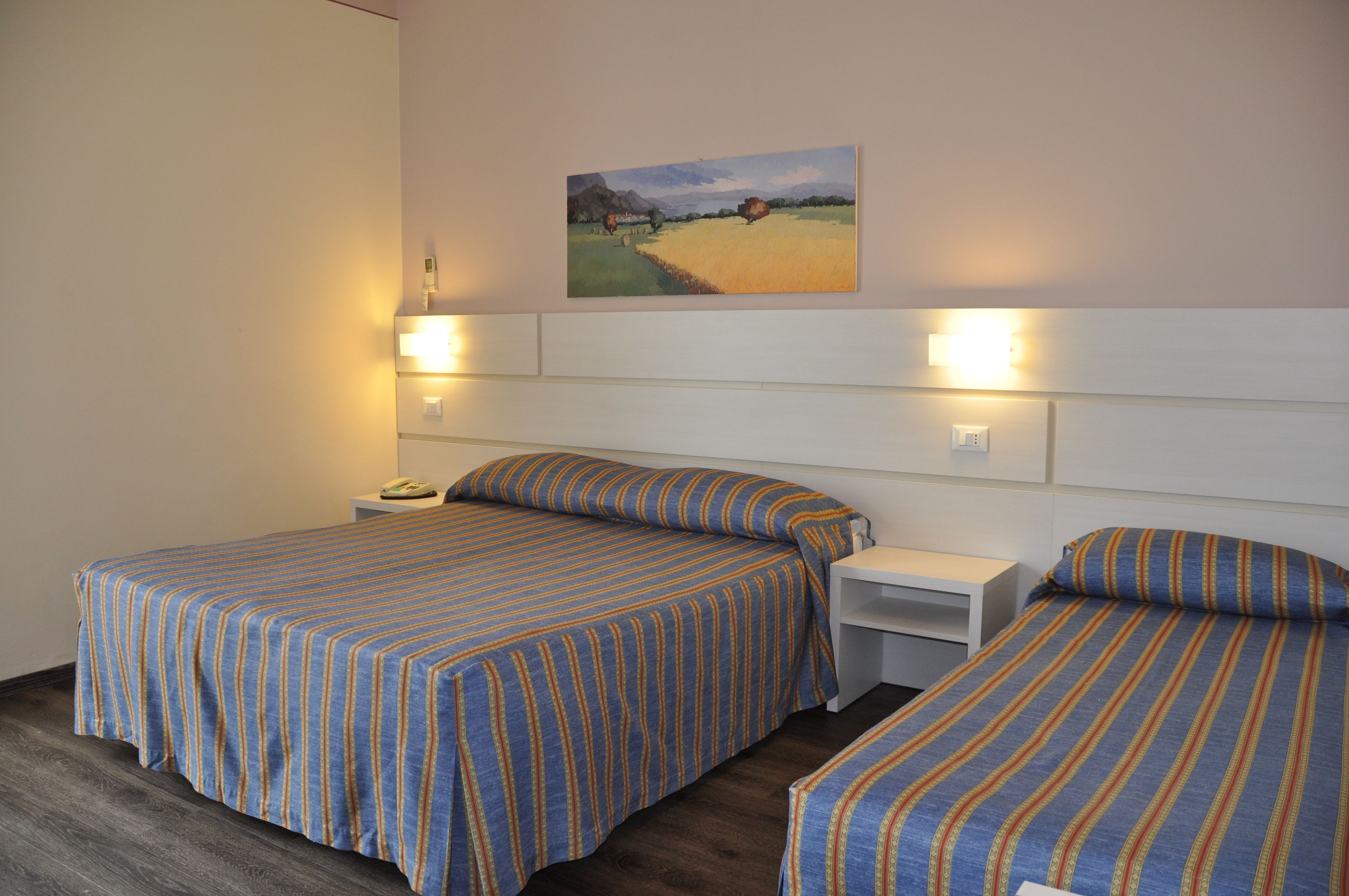 A hotel room with two beds, each with striped bedding, a painting on the wall, and bedside lamps.