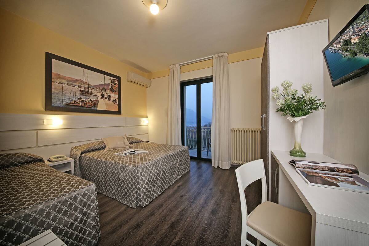 Een hotelkamer met twee bedden, een bureau, een stoel, een televisie en een balkon met uitzicht.