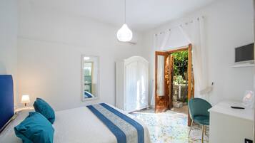 Un dormitorio con cama, escritorio, silla, televisión y puerta que da a un espacio al aire libre.