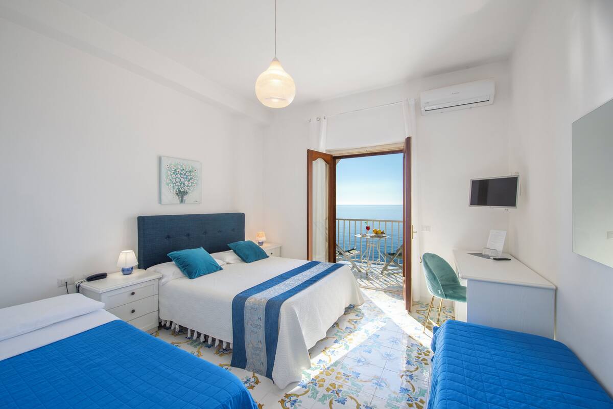 A hotel room with a bed, bedside table, lamp, and a view of the sea.