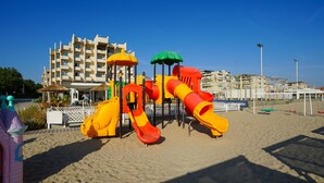 A beach playground with slides and climbing structures, set against a backdrop of a hotel and buildings. - Hotel Dasamo - Dada Hotels (Rimini)