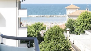 A coastal view from a balcony overlooking a beach with a rocky breakwater, a few boats, and a clear sky. - Hotel Dasamo - Dada Hotels (Rimini)