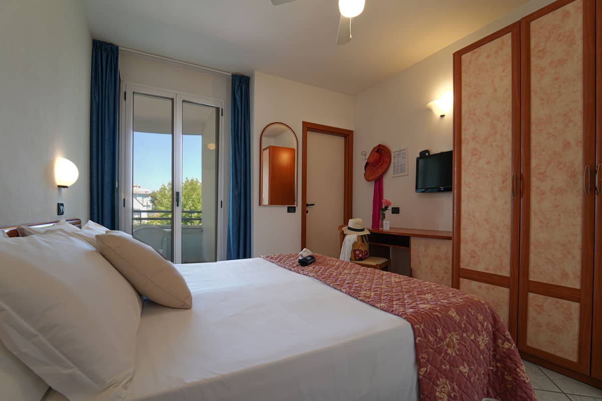 A hotel room with a bed, a desk, a chair, a TV, and a wardrobe.