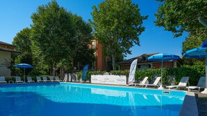 A swimming pool with lounge chairs and umbrellas, surrounded by trees and buildings. - Hotel Dasamo - Dada Hotels (Rimini)