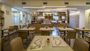 A restaurant with tables set for dining, a bar area with various items, and a stone wall in the background. - Hotel Villa Lalla (Rimini)