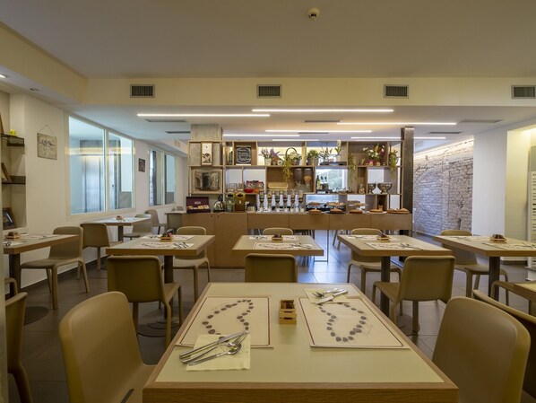 A restaurant with tables set for dining, a bar area with various items, and a stone wall in the background. - Hotel Villa Lalla (Rimini)