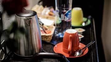 Bandeja de desayuno con una tetera de acero inoxidable, una taza roja, una lata de refresco, un vaso de zumo de naranja y un plato pequeño con una cuchara.