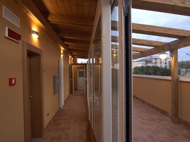 A corridor with wooden ceiling beams, tiled floor, and glass doors leading to rooms.