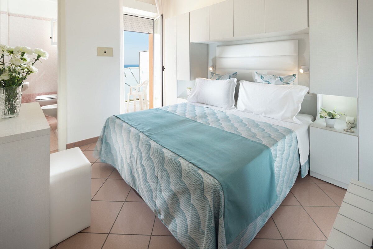 Un dormitorio con cama, mesitas de noche, un sillón y vistas al exterior.