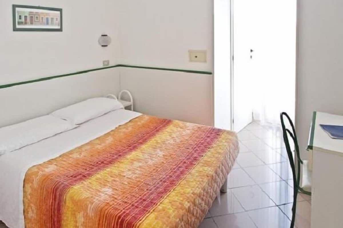 A bedroom with a bed, a chair, a desk, and a door.