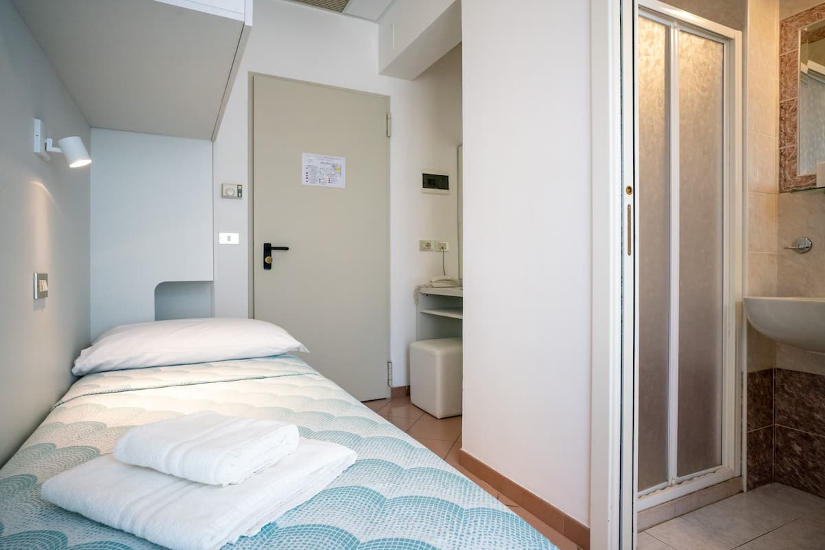 A bedroom with a bed, a bathroom with a shower, and a door leading to a hallway.