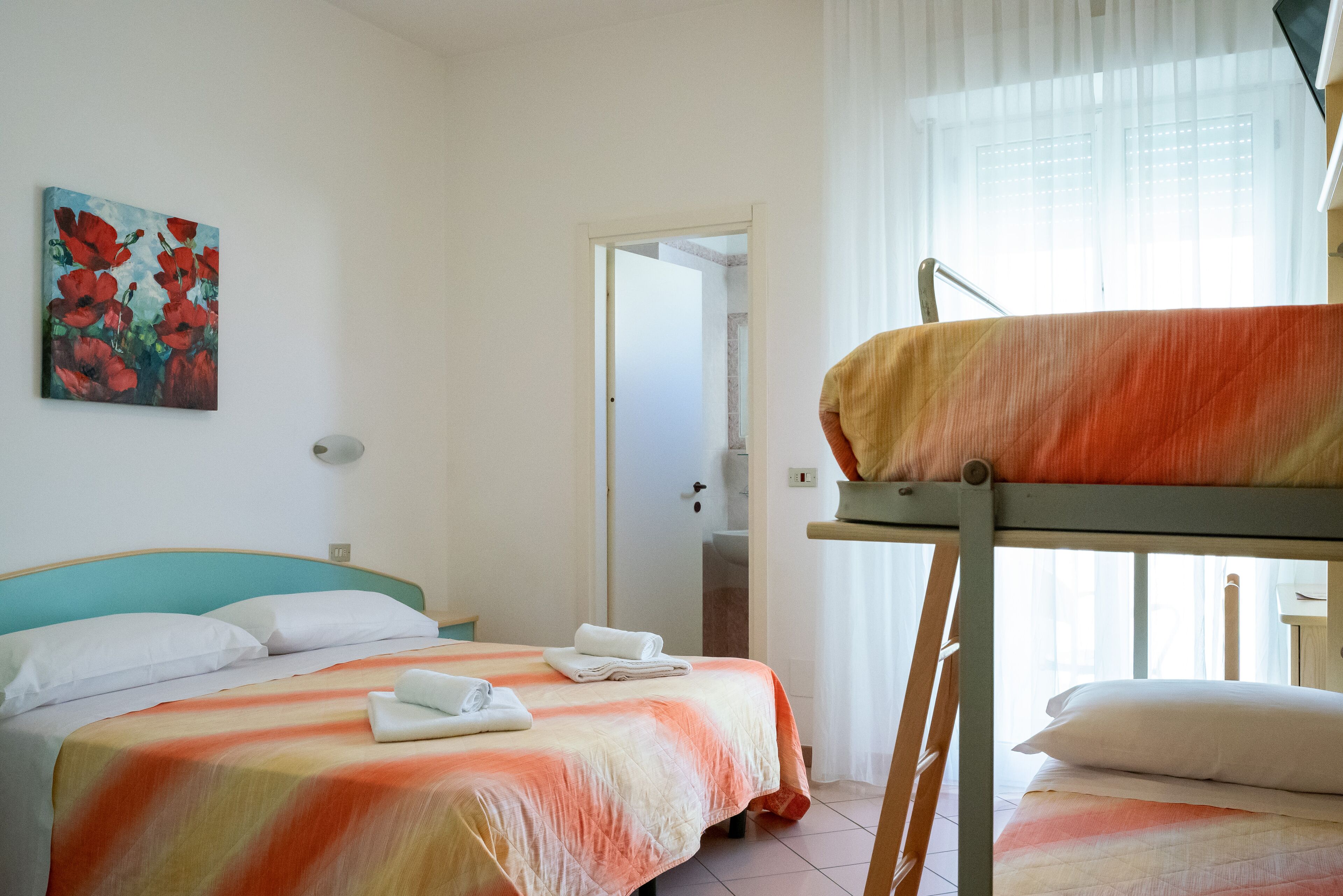 A room with a bed, a bunk bed, a painting, and a door leading to another room.