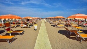 Una playa con filas de tumbonas y sombrillas naranjas.