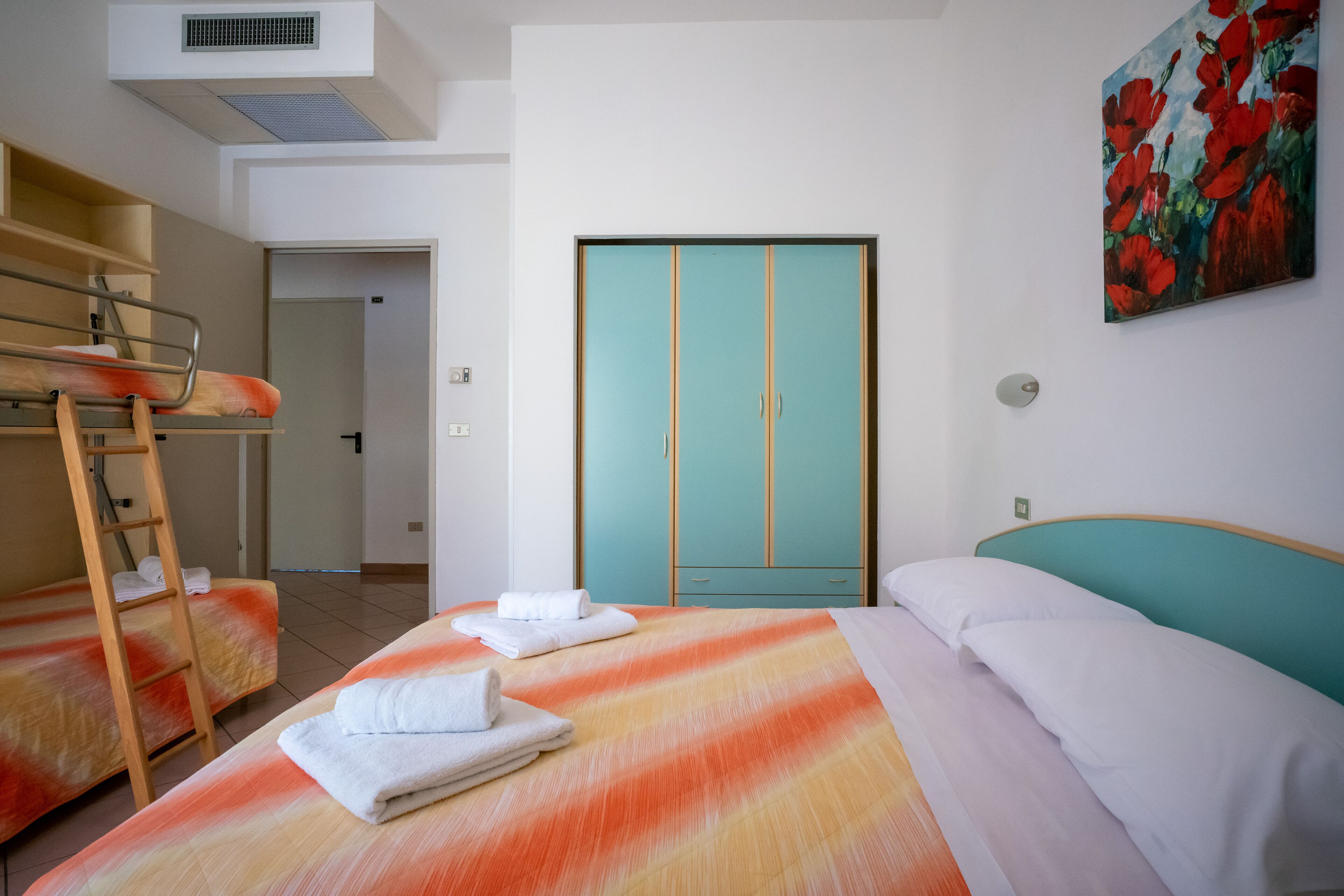 Habitación de hotel con literas, un armario color aguamarina y un cuadro de flores rojas.