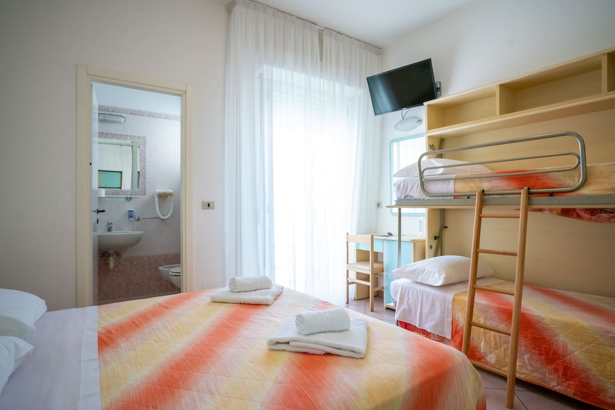 A hotel room with two beds, a TV, a bathroom, and a desk.