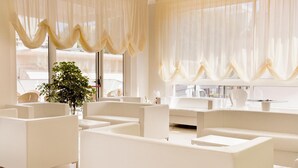 Un vestíbulo moderno y minimalista con mobiliario blanco y grandes ventanales con cortinas de gasa.