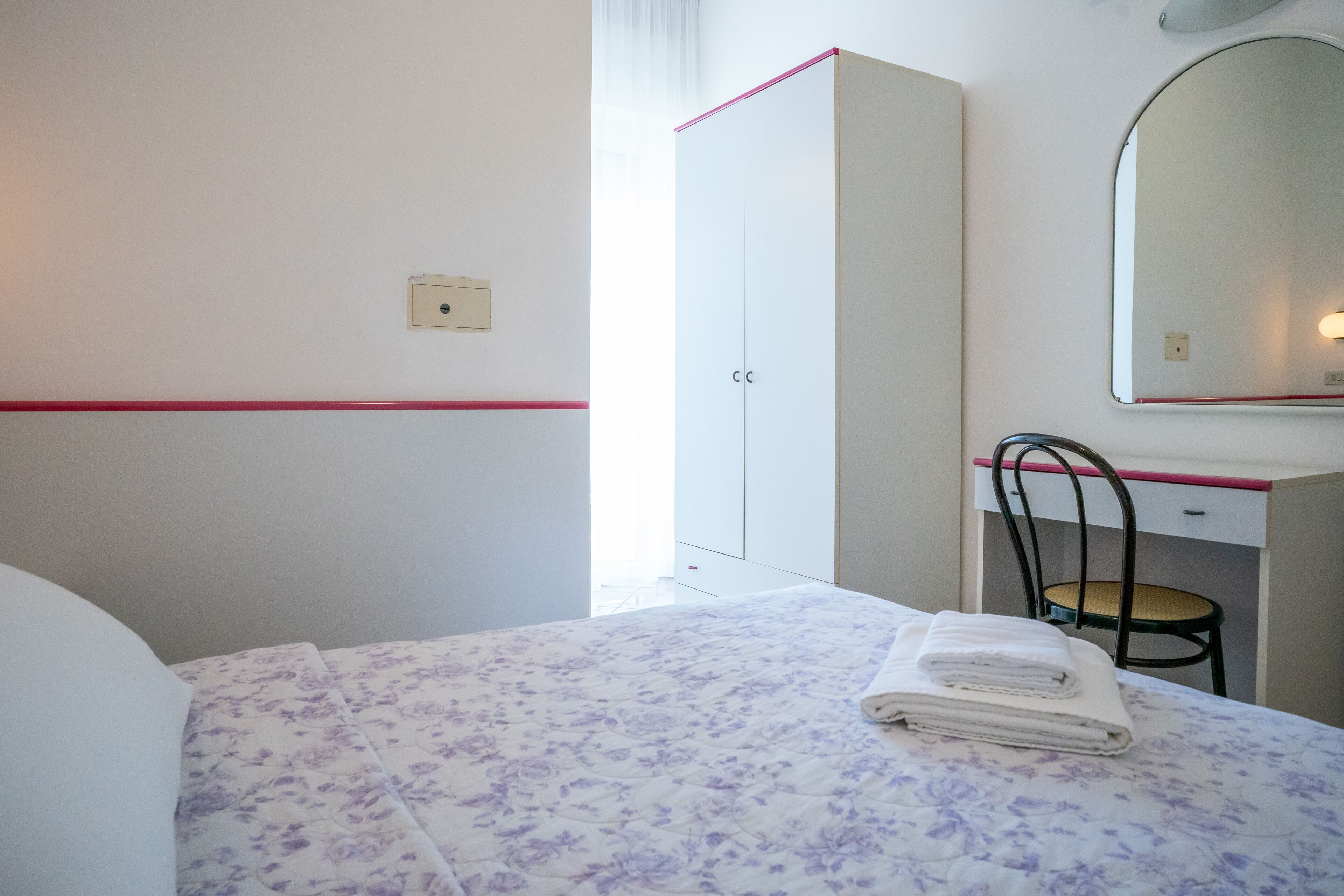 A hotel room with a bed, a wardrobe, a desk, and a chair.