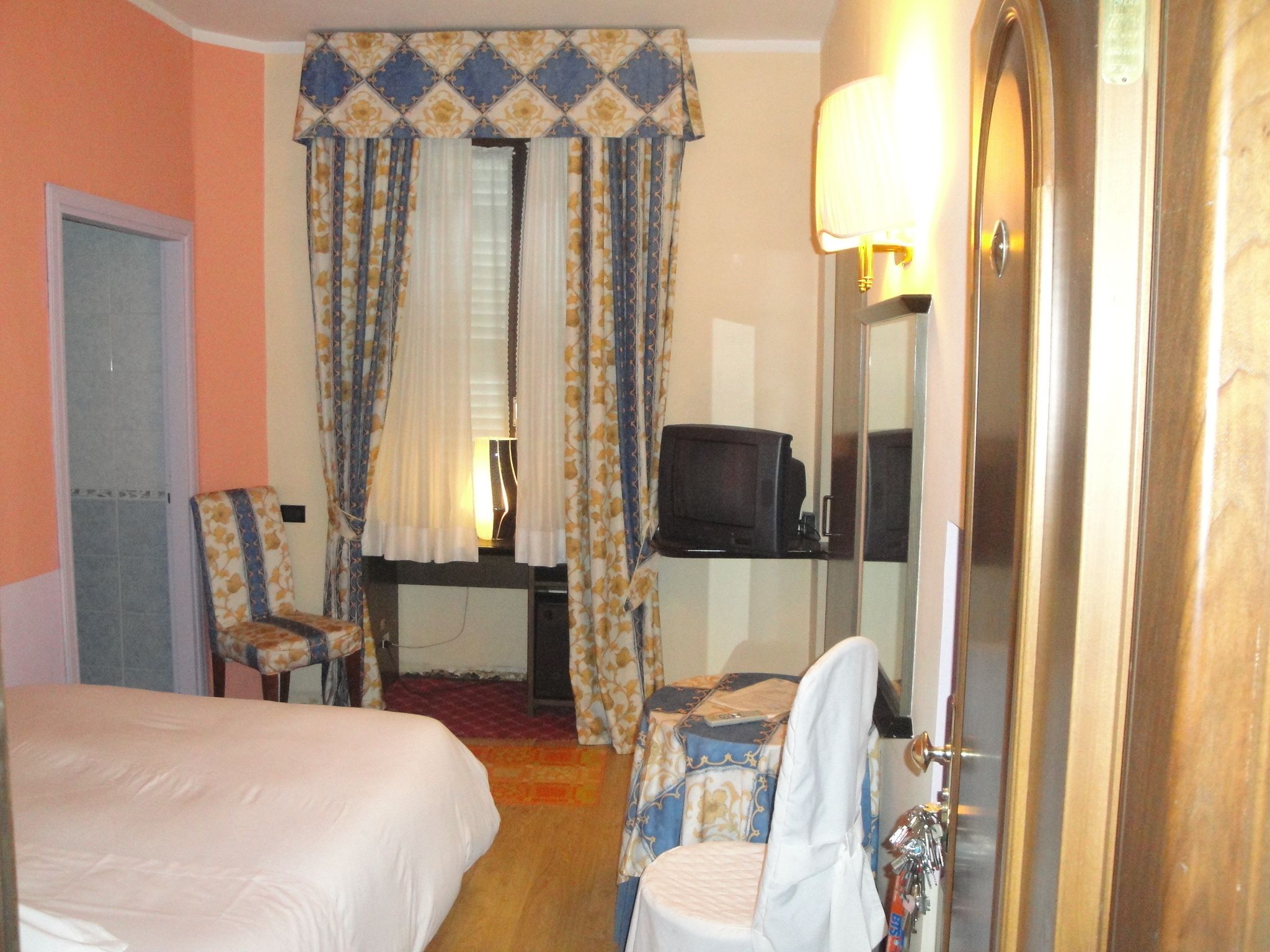 A hotel room with a bed, a chair, a desk with a television, and a mirror.