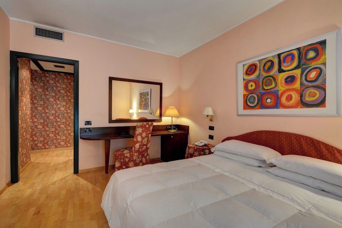 Una camera d'albergo con un letto, una scrivania, una sedia e un quadro appeso al muro.