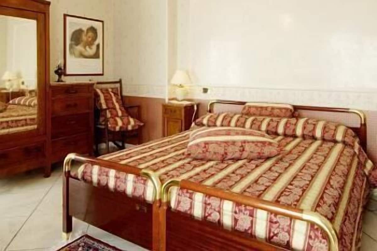 A bedroom with a wooden bed, a nightstand, a chair, a mirror, and a framed picture on the wall.