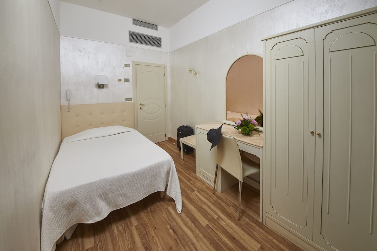 A hotel room with a bed, a desk with a chair, a wardrobe, and a mirror.