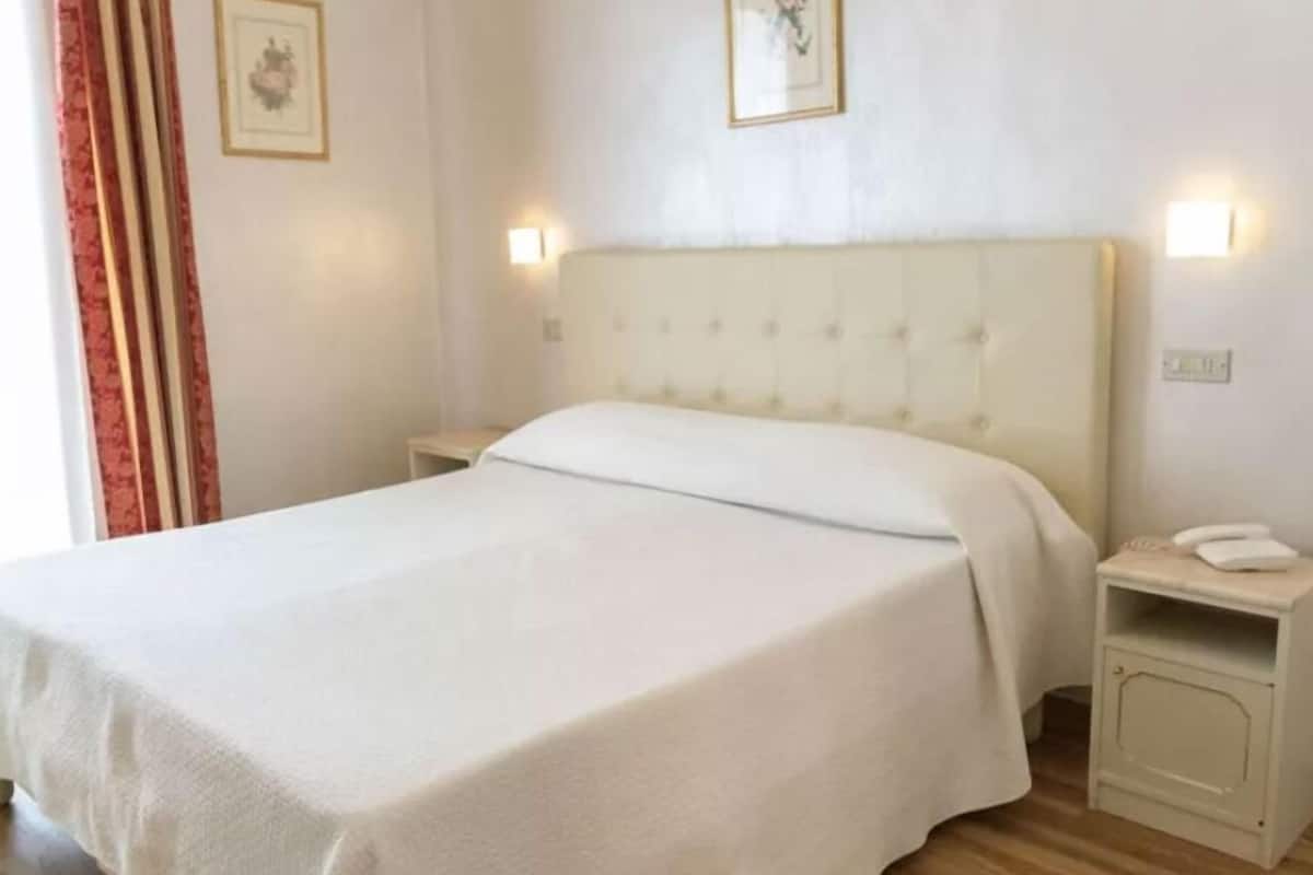 A hotel room with a large bed, bedside tables, and wall-mounted lamps.