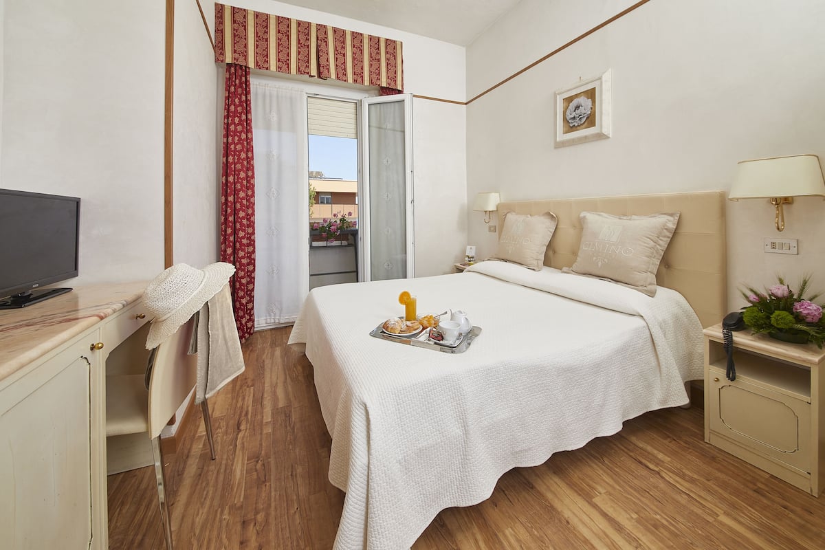 A hotel room with a bed, bedside tables, a desk with a TV, and a balcony with a red curtain.