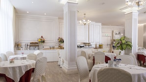 A formal dining room with white tables and chairs, a central column, and a chandelier. - Hotel Vienna Ostenda (Rimini)