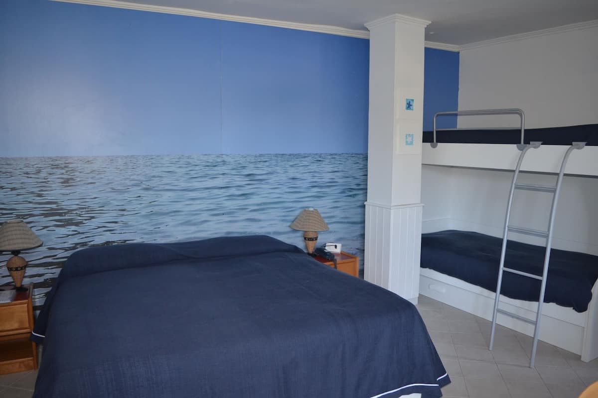 A room with a bunk bed, a nightstand with a lamp, and a wall mural of the ocean.