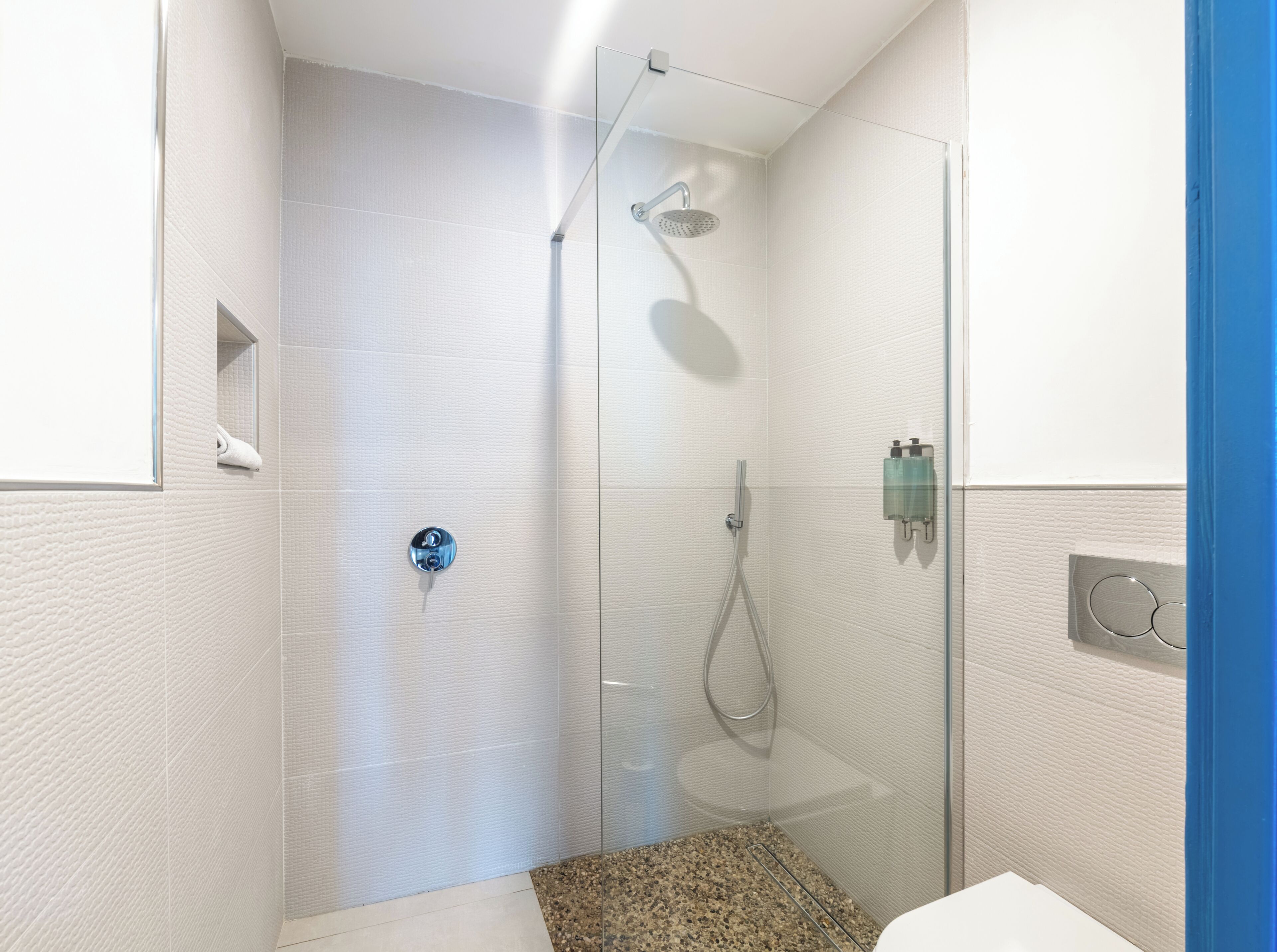 Un moderno box de ducha con puerta de vidrio, un cabezal de ducha manual y un grifo empotrado en la pared.