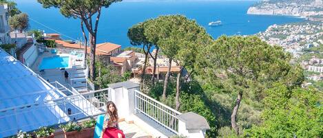 A terrace with a pool, overlooking a coastal town and the sea.