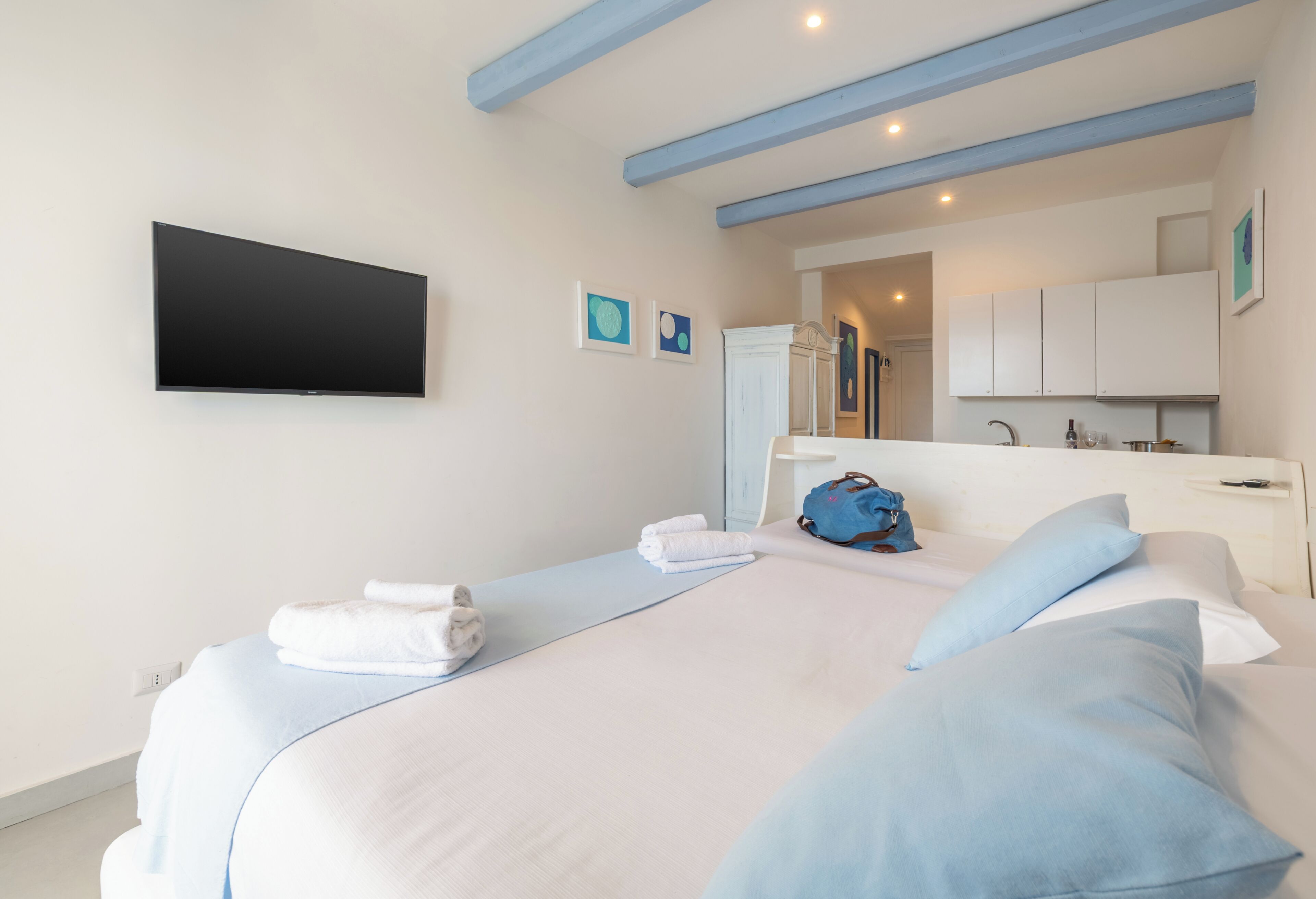 A hotel room with a bed, a flat-screen TV, a bathroom with a mirror, and a kitchenette.