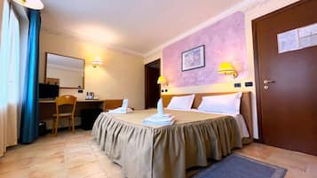 Una camera d'albergo con un letto, una scrivania con un computer, una sedia e una lampada da scrivania.