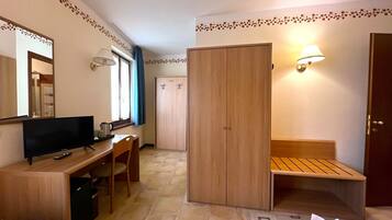Habitación de hotel con una cama, un escritorio con silla, televisión, armario y un banco.