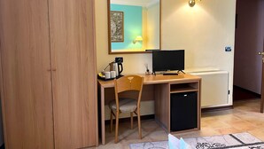 A hotel room with a wooden desk, a chair, a television, a coffee maker, a small refrigerator, and a wall-mounted lamp. - Hotel Susa (Susa)