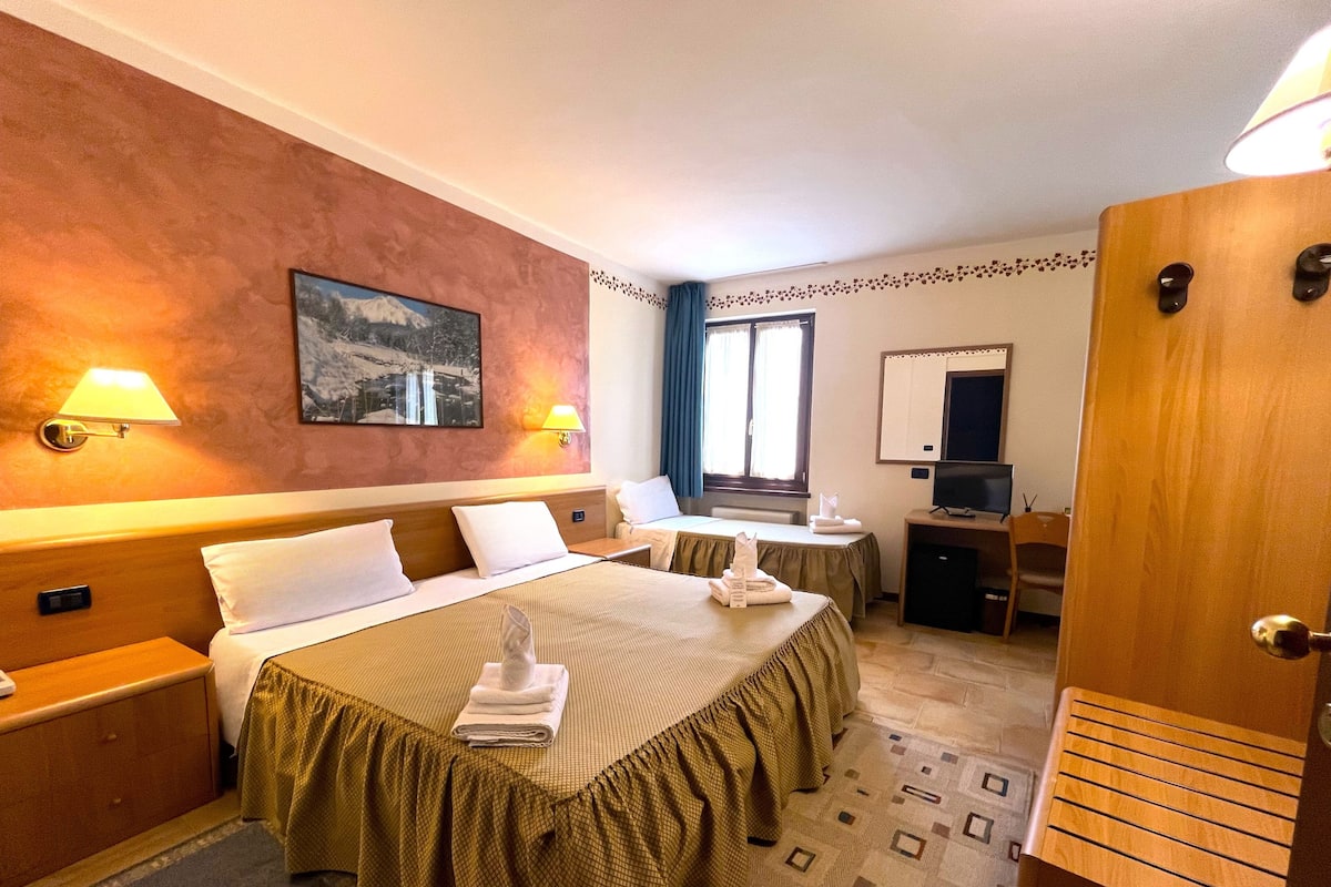A hotel room with two beds, a desk, a TV, and a painting on the wall.
