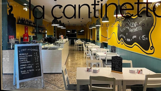 A restaurant interior with a chalkboard menu, white tables, and hanging pendant lights. - Hotel Susa (Susa)