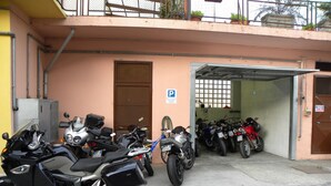 A parking area with several motorcycles and bicycles, a building entrance, and a parking sign. - Hotel Susa (Susa)