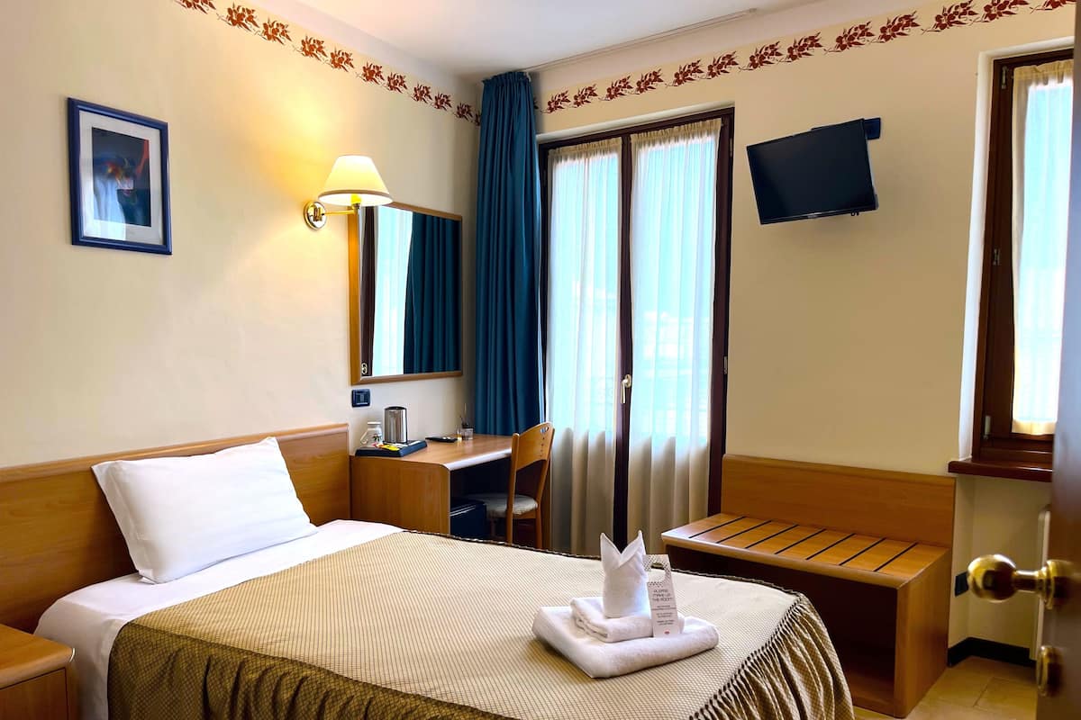 A hotel room with a bed, a desk, a chair, a TV, and a window with curtains.