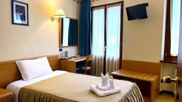 A hotel room with a bed, a desk, a chair, a TV, and a window with curtains.