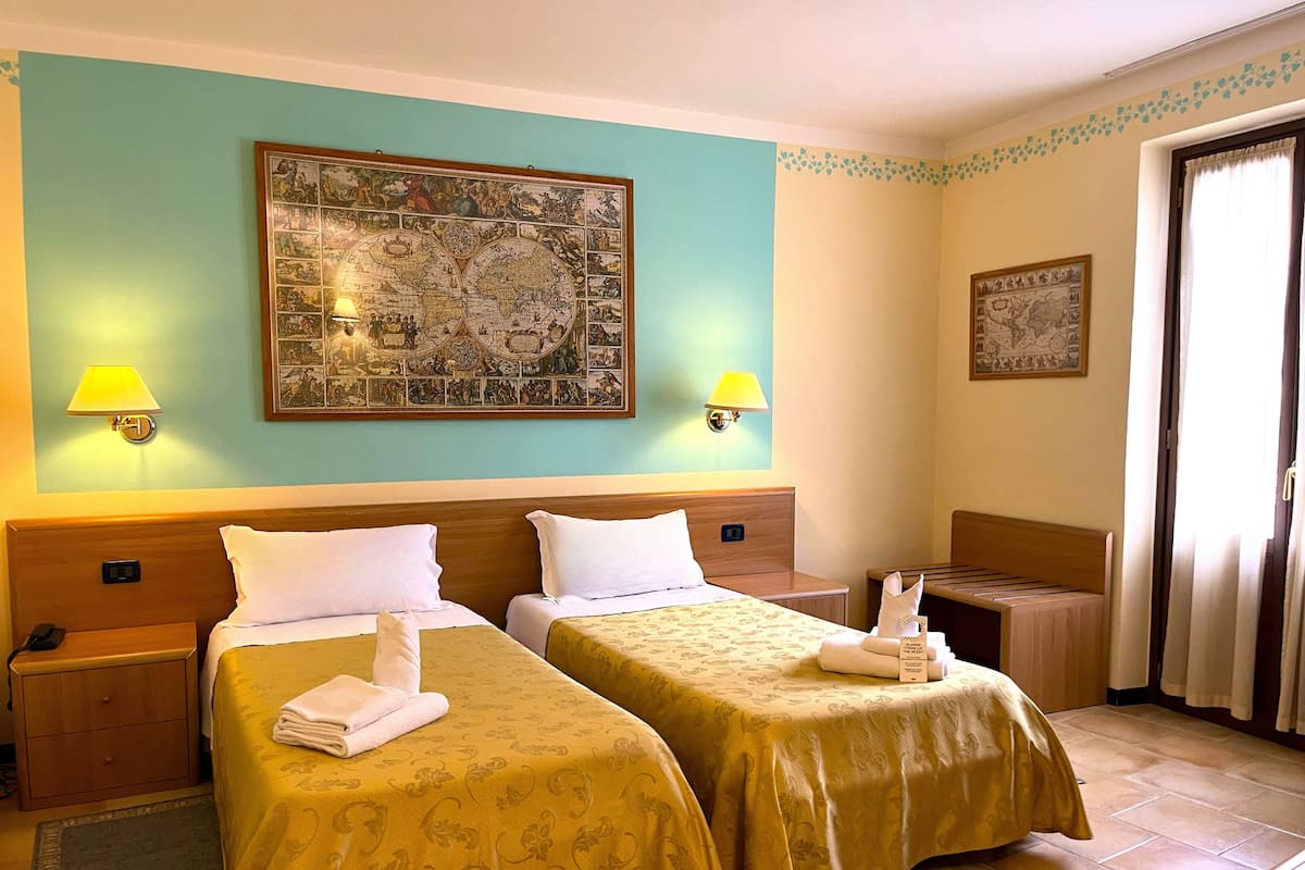 A hotel room with two beds, a large map on the wall, and two bedside lamps.