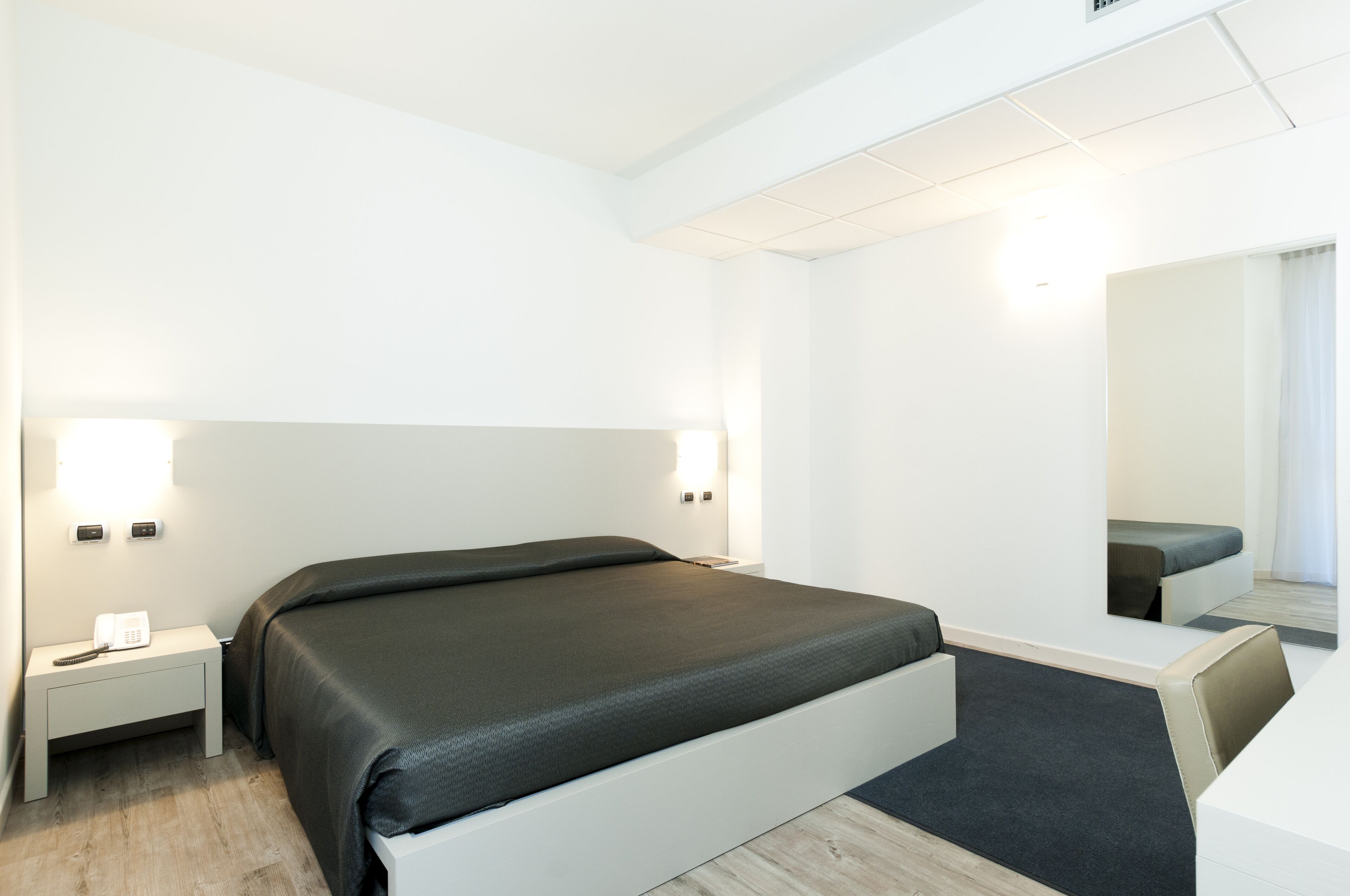 Et moderne hotelværelse med en stor seng, sengeborde og et spejl.