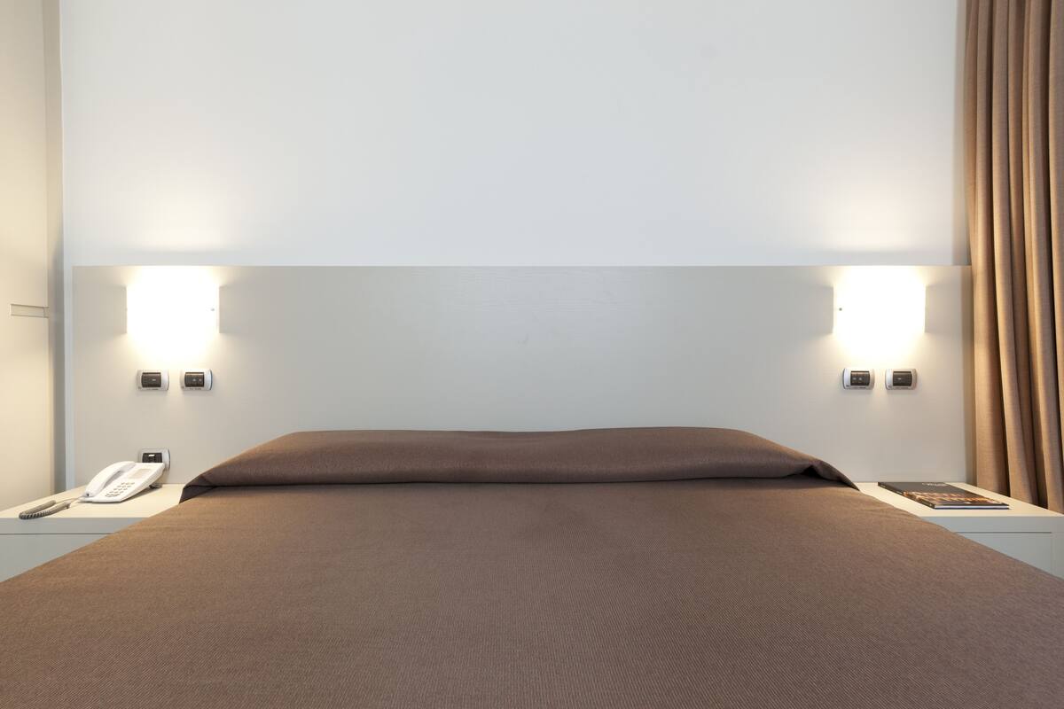 A hotel room with a large bed, two bedside lamps, a telephone, and a book on the nightstand.