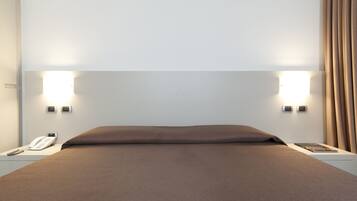 Quarto de hotel com uma cama grande, duas luminárias de cabeceira, um telefone e um livro na mesa de apoio.